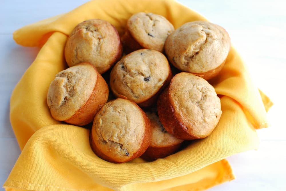 A bowl lined with a yellow napkin filled with a bunch of banana protein muffins.