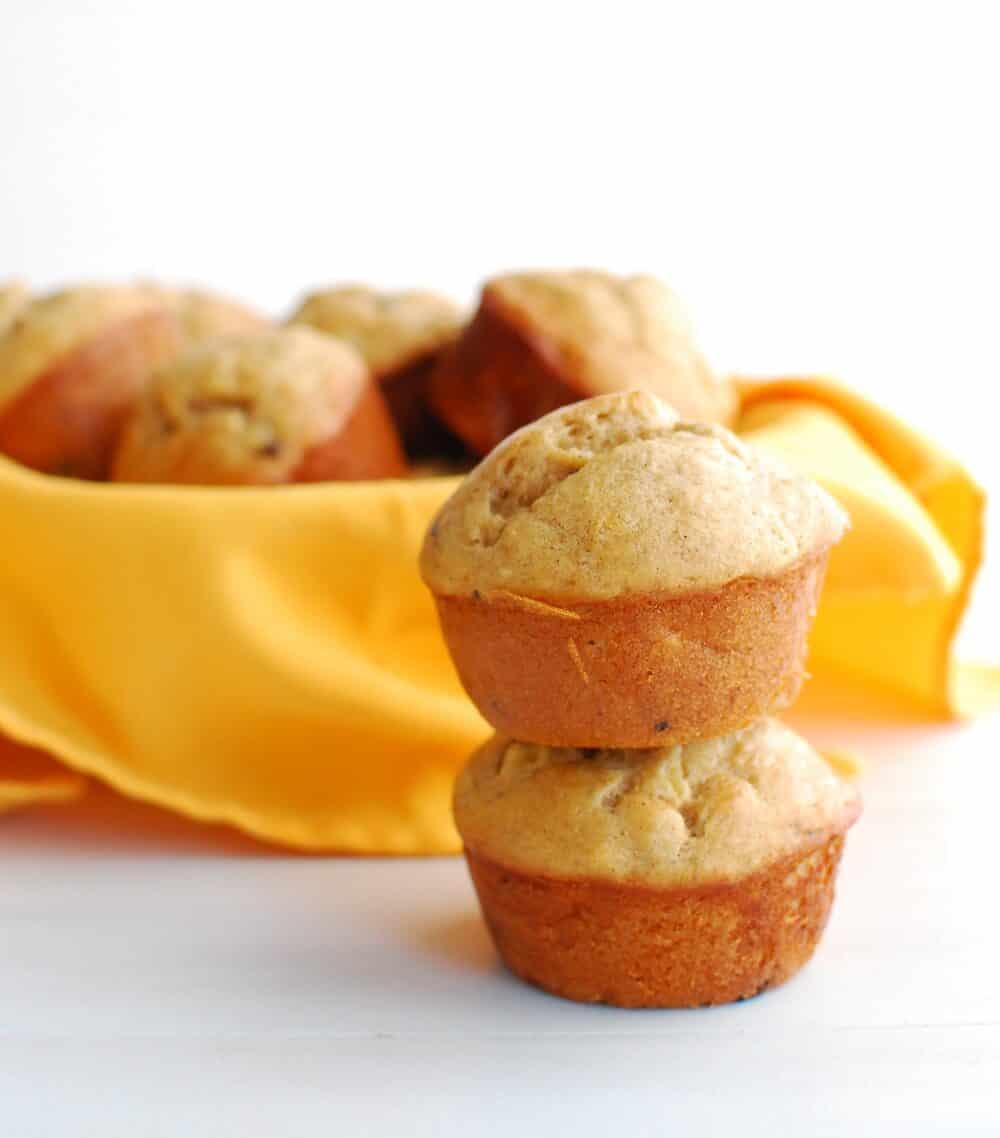 Two banana muffins stacked up next to a bowl full of muffins.