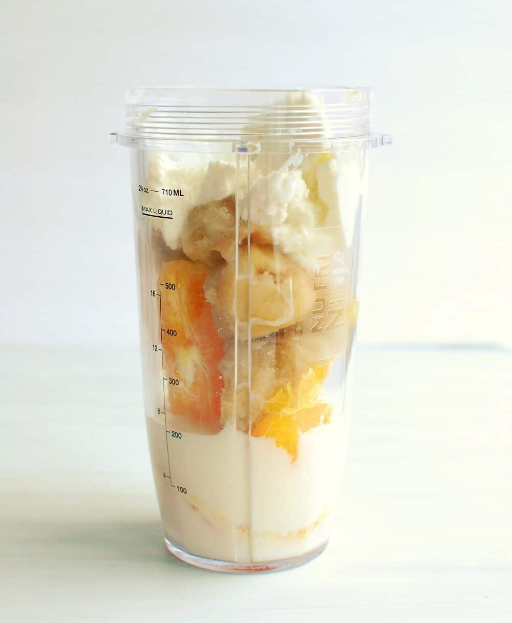 a blender cup full of banana, orange, yogurt, and milk