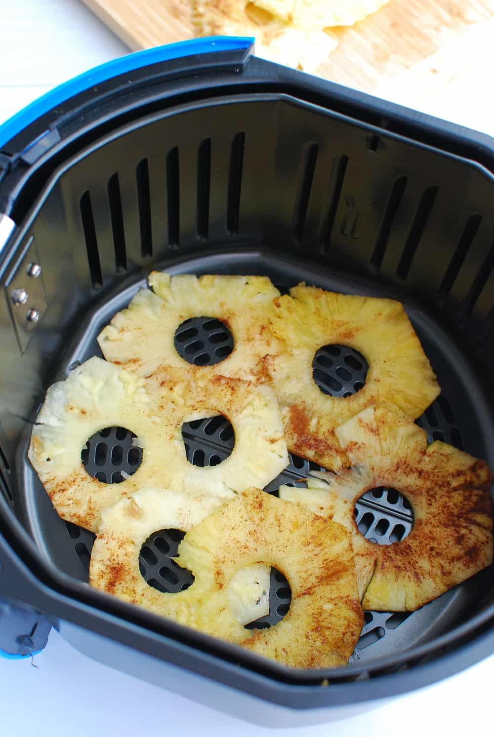 pineapple being put in an air fryer basket before cooking