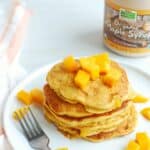 a stack of mango pancakes on a white plate, topped with extra mango