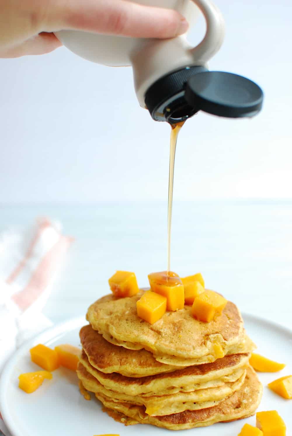 a woman pouring maple syrup onto a stack of pancakes