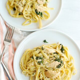 two plates with pesto salmon pasta, alongside two forks and a cloth napkin