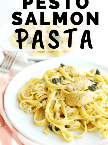 a plate full of pesto salmon pasta next to a striped napkin