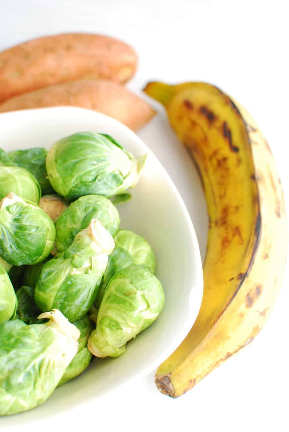 a bowl of brussels sprouts, a plantain, and two sweet potatoes