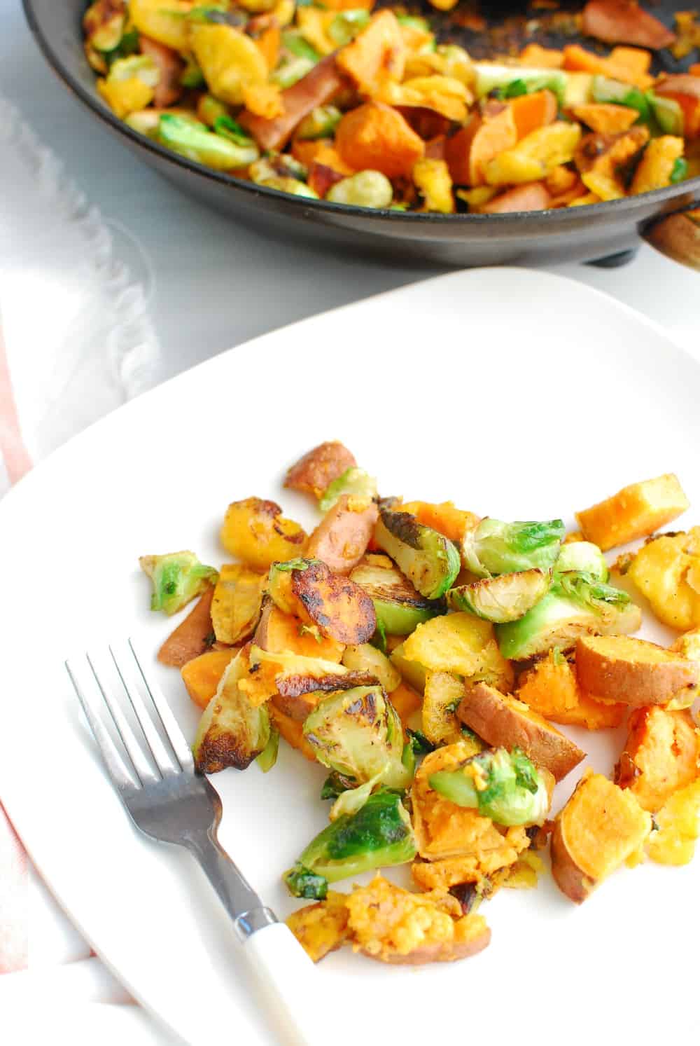 A plate with sweet potato brussels sprouts hash next to a fork and a skillet