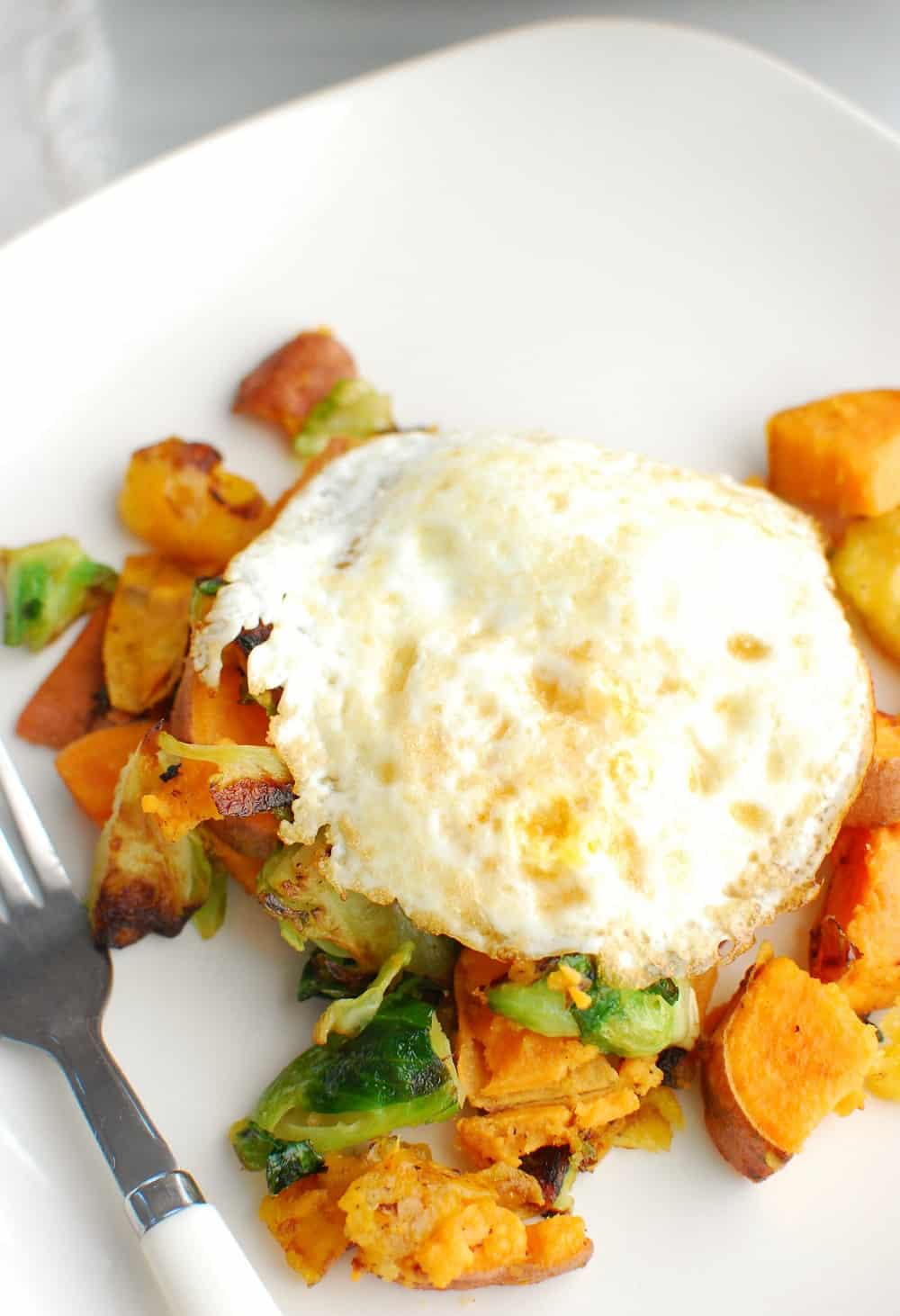 a plate with sweet potatoes, brussels sprouts, plantains, and an egg on top