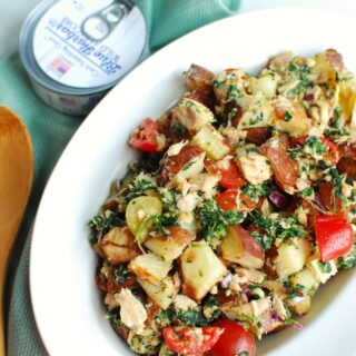 a bowl of tuna potato salad next to a can and blue napkin