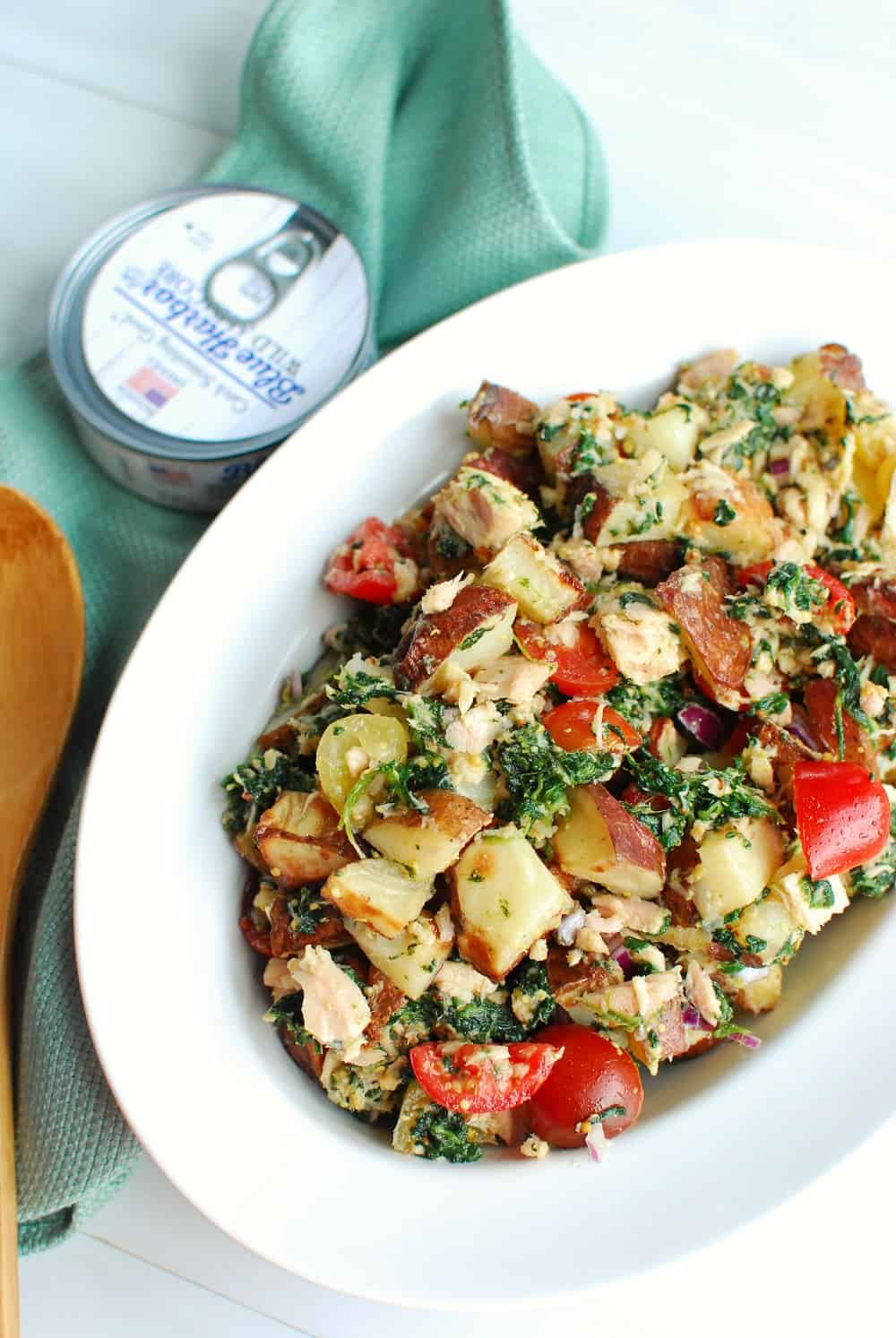 a bowl of tuna potato salad next to a can and blue napkin