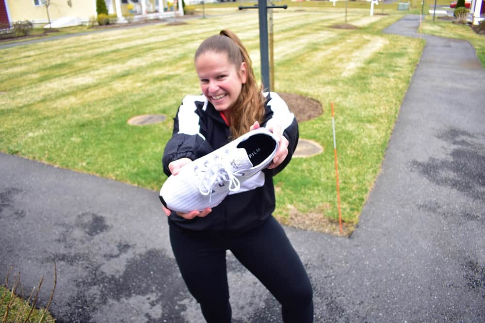 a woman outside holding a sneaker towards the camera