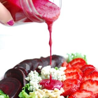 a woman pouring homemade beet salad dressing onto a salad