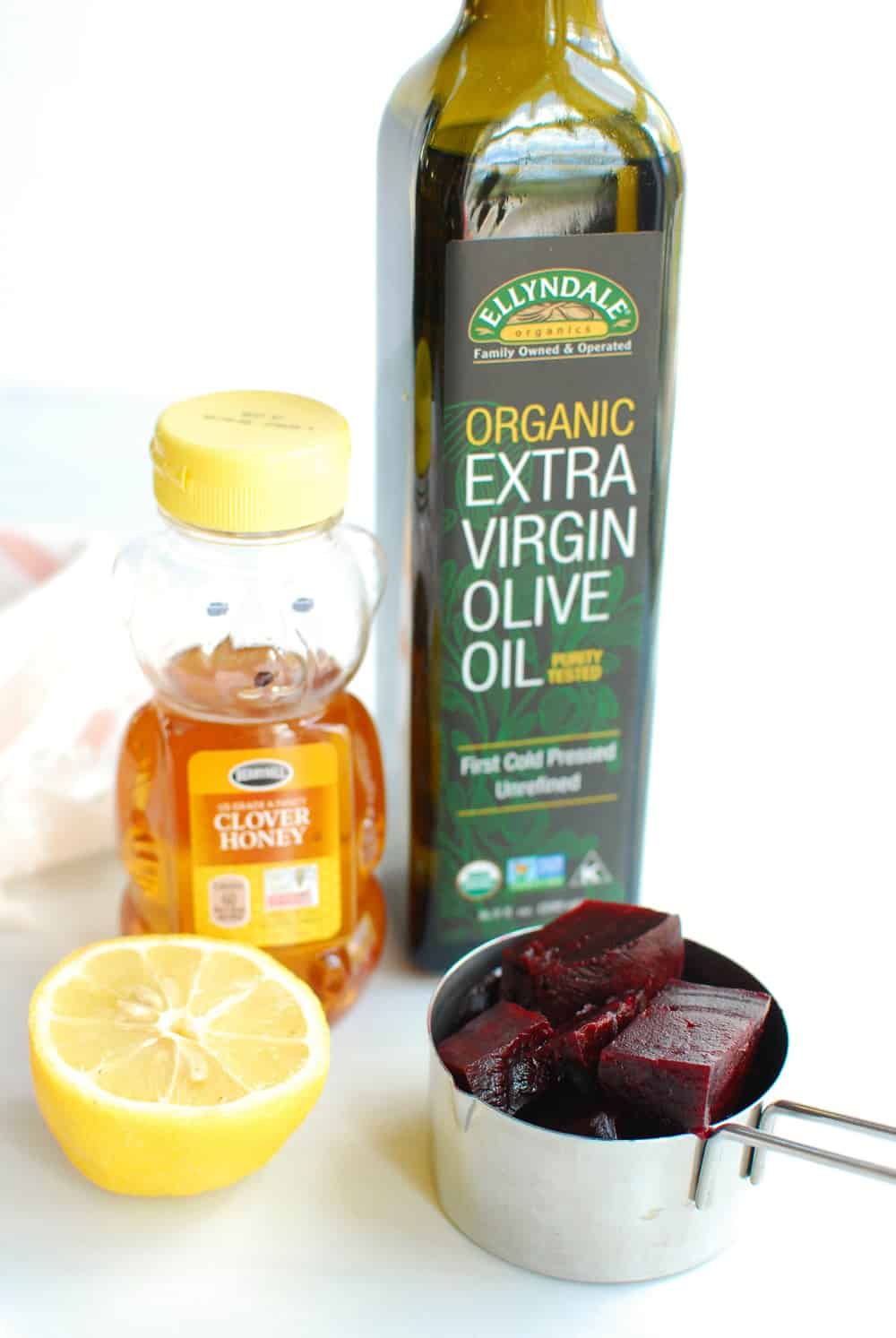 a lemon, a container of honey, a bottle of olive oil, and a measuring cup with chopped beets