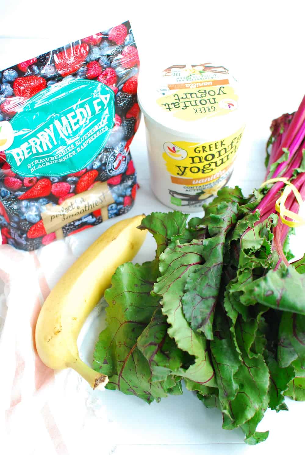 a bag of frozen berries, a container of greek yogurt, a banana, and a bunch of beet greens