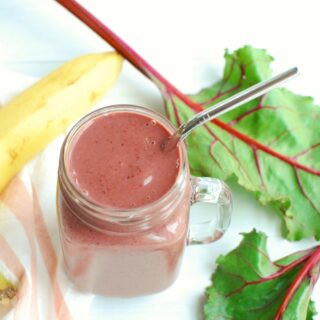 a mason jar with a banana, berry, and beet green smoothie in it, next to a banana and some raw fresh beet greens