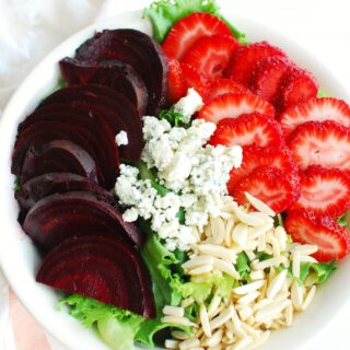 a white bowl filled with a strawberry beet salad next to a pink and white napkin