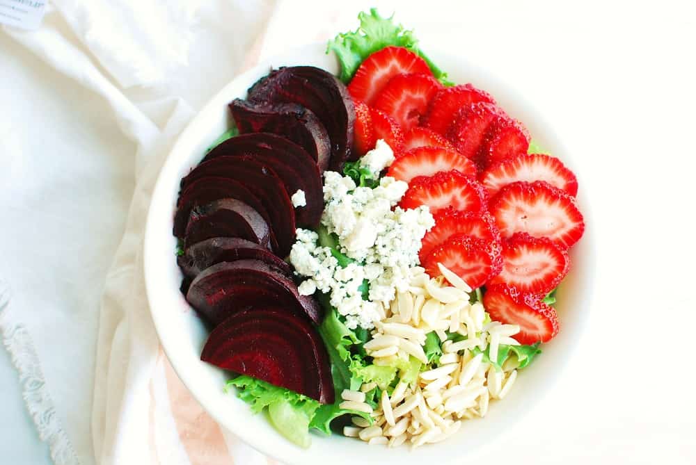 a beet strawberry salad in a white bowl next to a cloth napkin