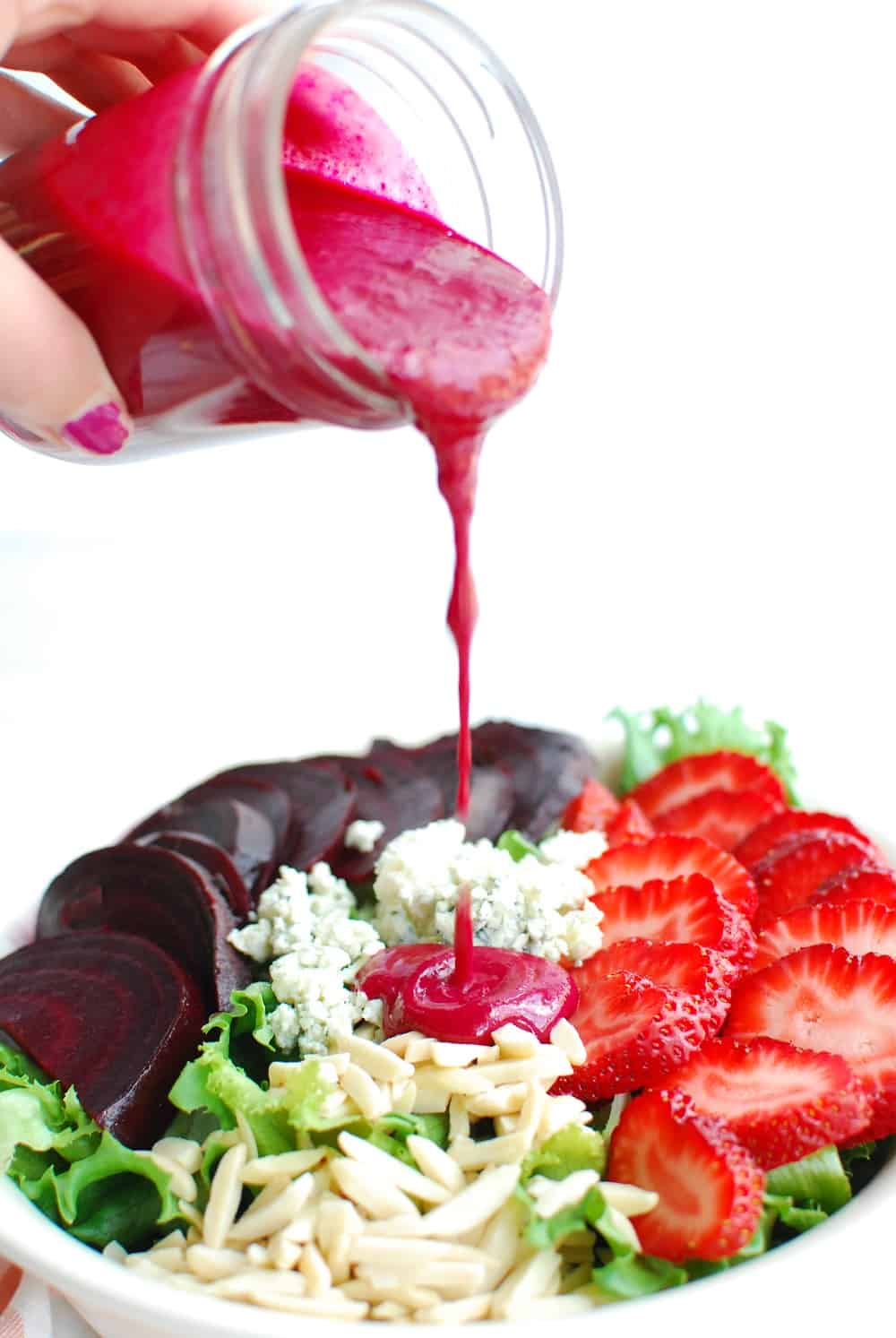 a woman pouring dressing onto a strawberry beet salad