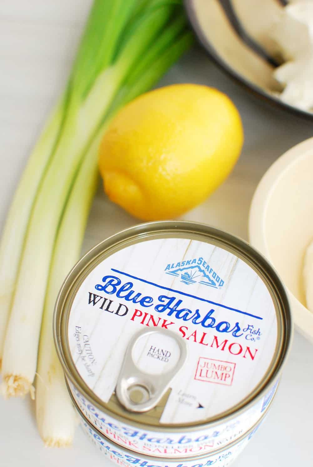 two cans of salmon next to green onions and a lemon