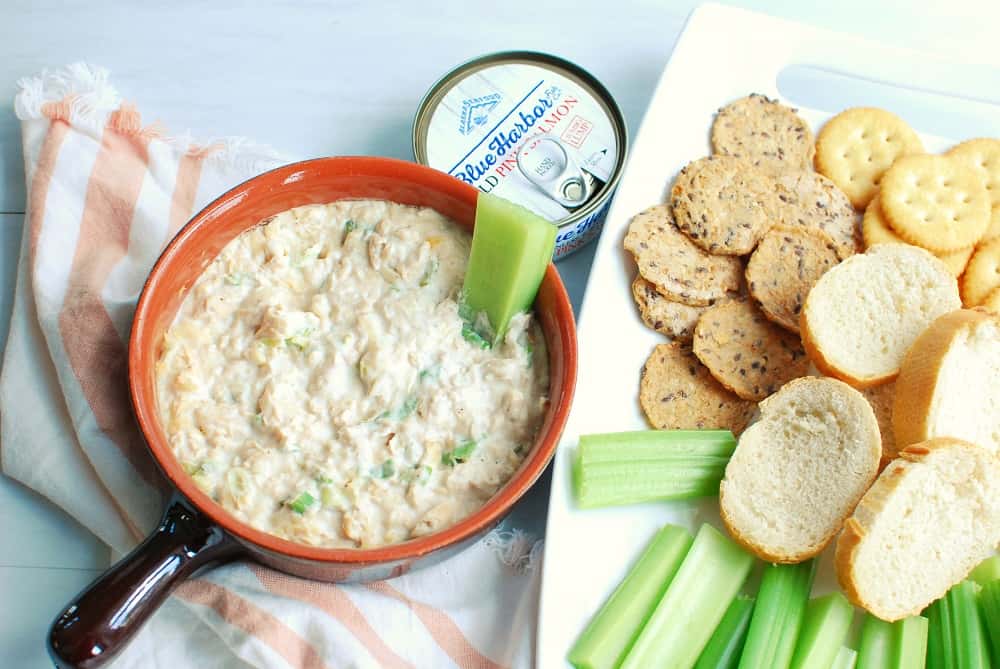 Hot version of canned salmon dip in a ramekin, next to crackers, celery, and baguettes