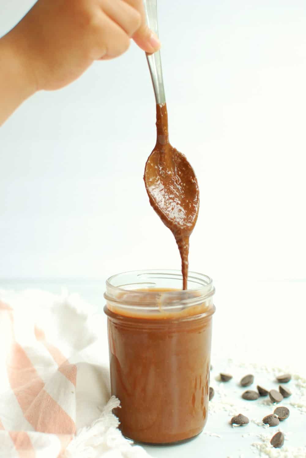 a person picking up a spoon that has chocolate nut butter dripping off the end into a jar