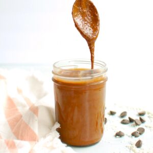 A jar of chocolate macadamia nut butter with a spoon dunked into it.