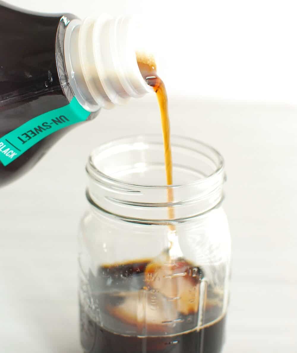 a person pouring cold brew coffee over ice in a mason jar