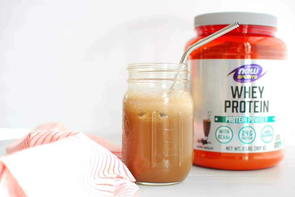 a mason jar with cold brew protein coffee, next to a container of protein powder and a pink napkin