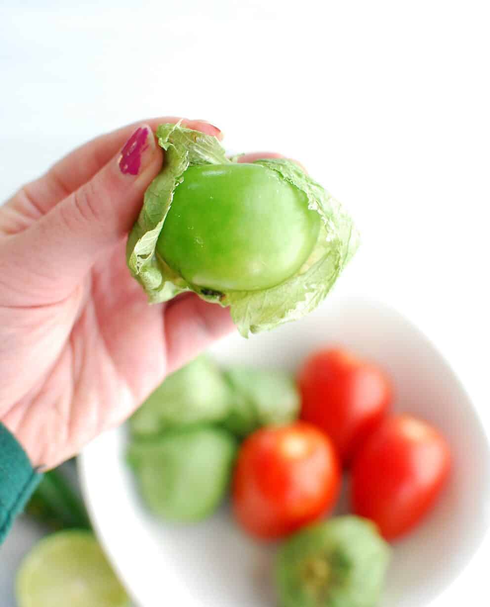 a woman holding a tomatillo, peeling back its husk