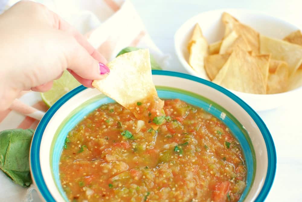 a woman dipping a tortilla chip into a bowl of tomatillo and tomato salsa