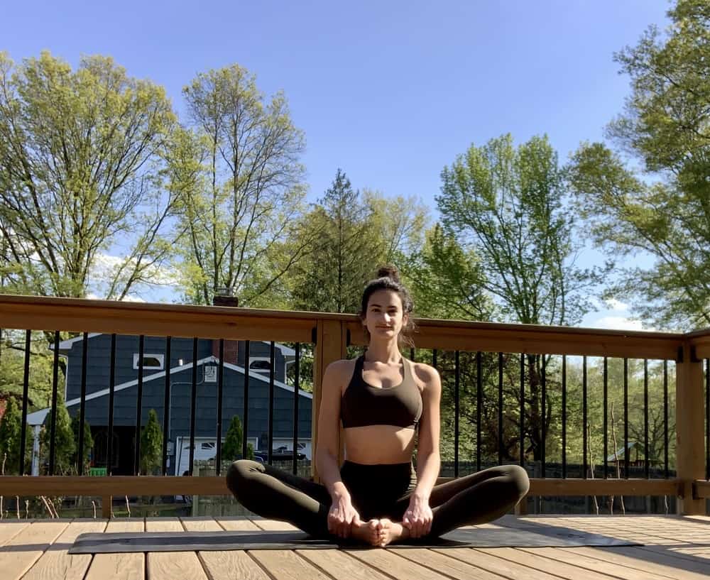 a woman doing the butterfly yoga pose outdoors on a deck