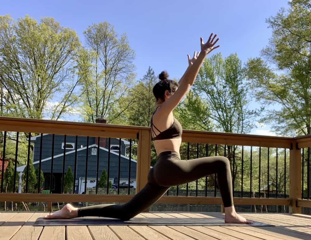 a woman doing a low lunge yoga pose for runners while outdoors on a deck