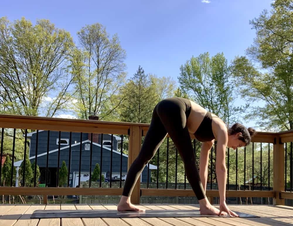 a woman doing a pyramid yoga pose for runners while outdoors on a deck