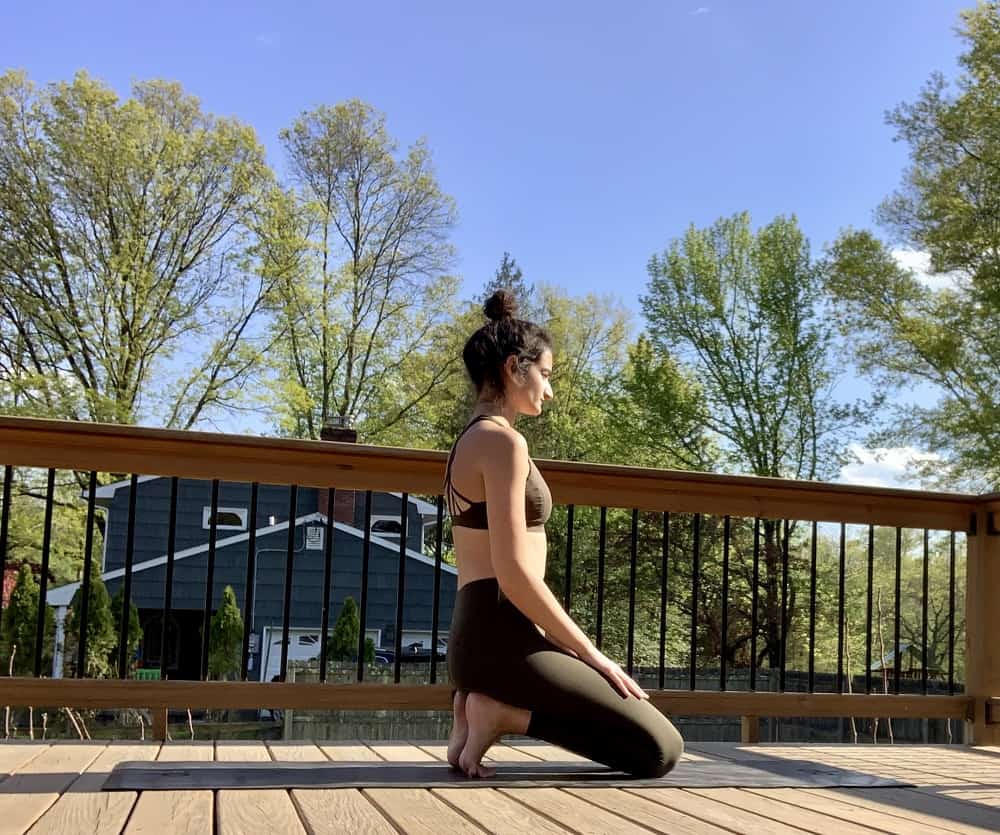 a woman doing a thunderbolt yoga pose with tucked toes outdoors on a deck