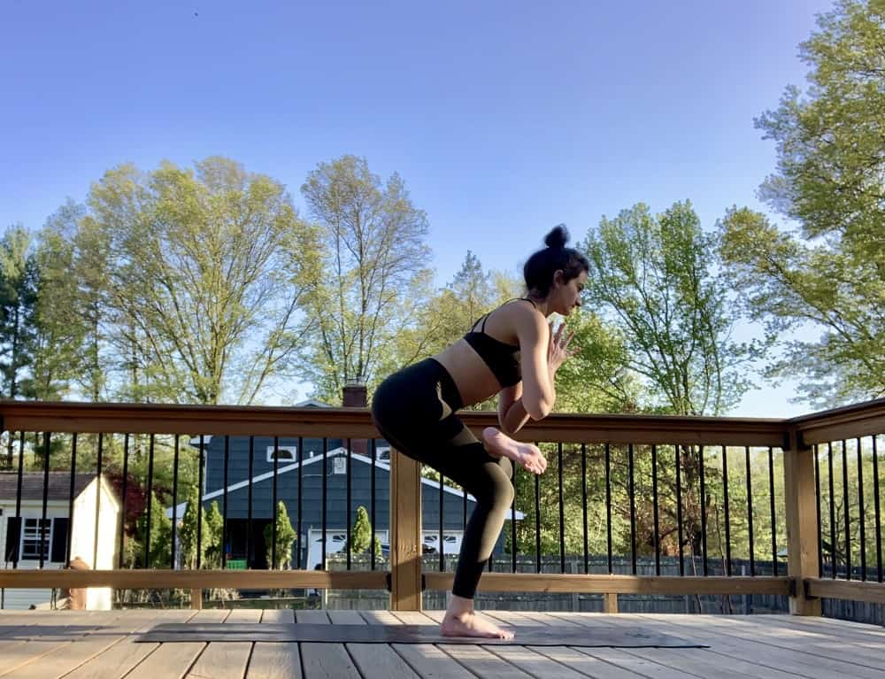 a woman doing a standing figure four yoga post outdoors on a deck