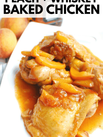peach whiskey chicken on a white platter next to two peaches and a bottle of whiskey