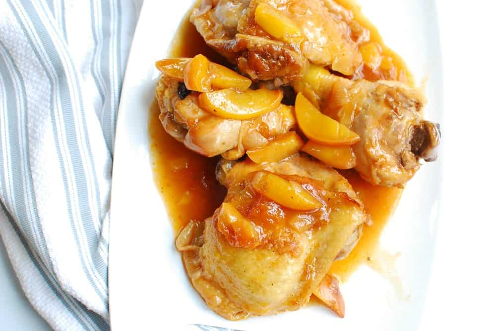 a white platter with whiskey peach chicken next to a striped napkin