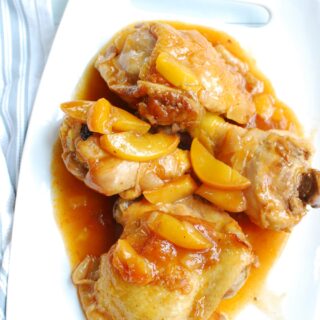 a white plate with peach whisky chicken next to a napkin