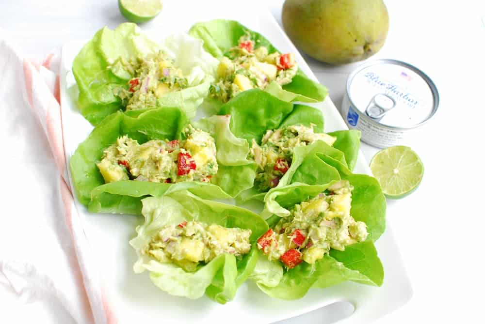 a white platter with six tuna lettuce wraps next to a can of tuna and a mango