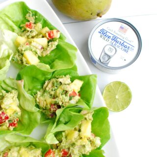 several tropical tuna lettuce wraps on a white serving platter next to a can of tuna and a mango