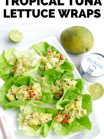 several tropical tuna lettuce wraps on a white serving platter next to a can of tuna and a mango