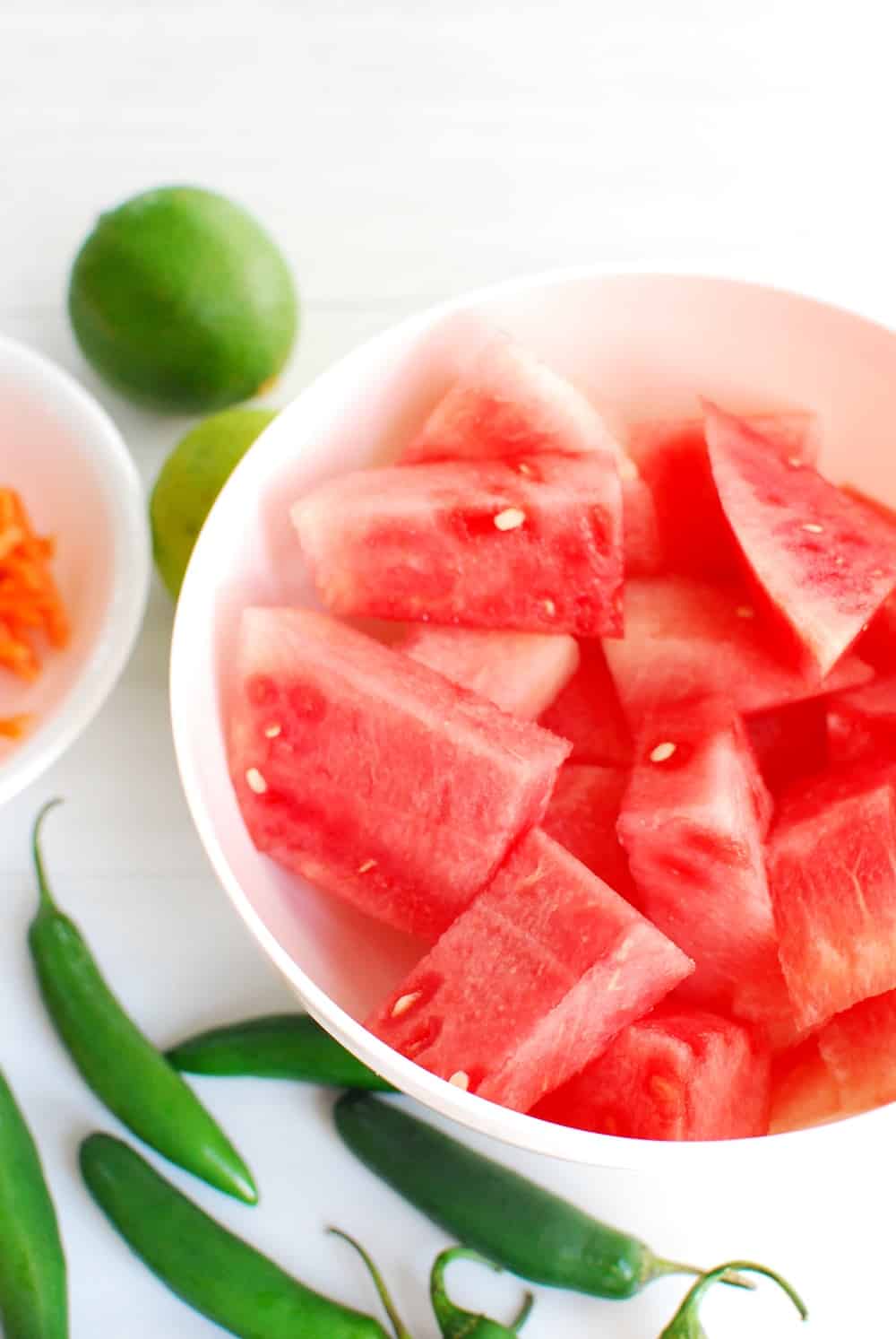 a bowl full of chopped watermelon next to some serrano peppers and a lime