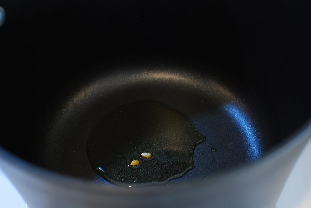 a pot with olive oil and two popcorn kernels