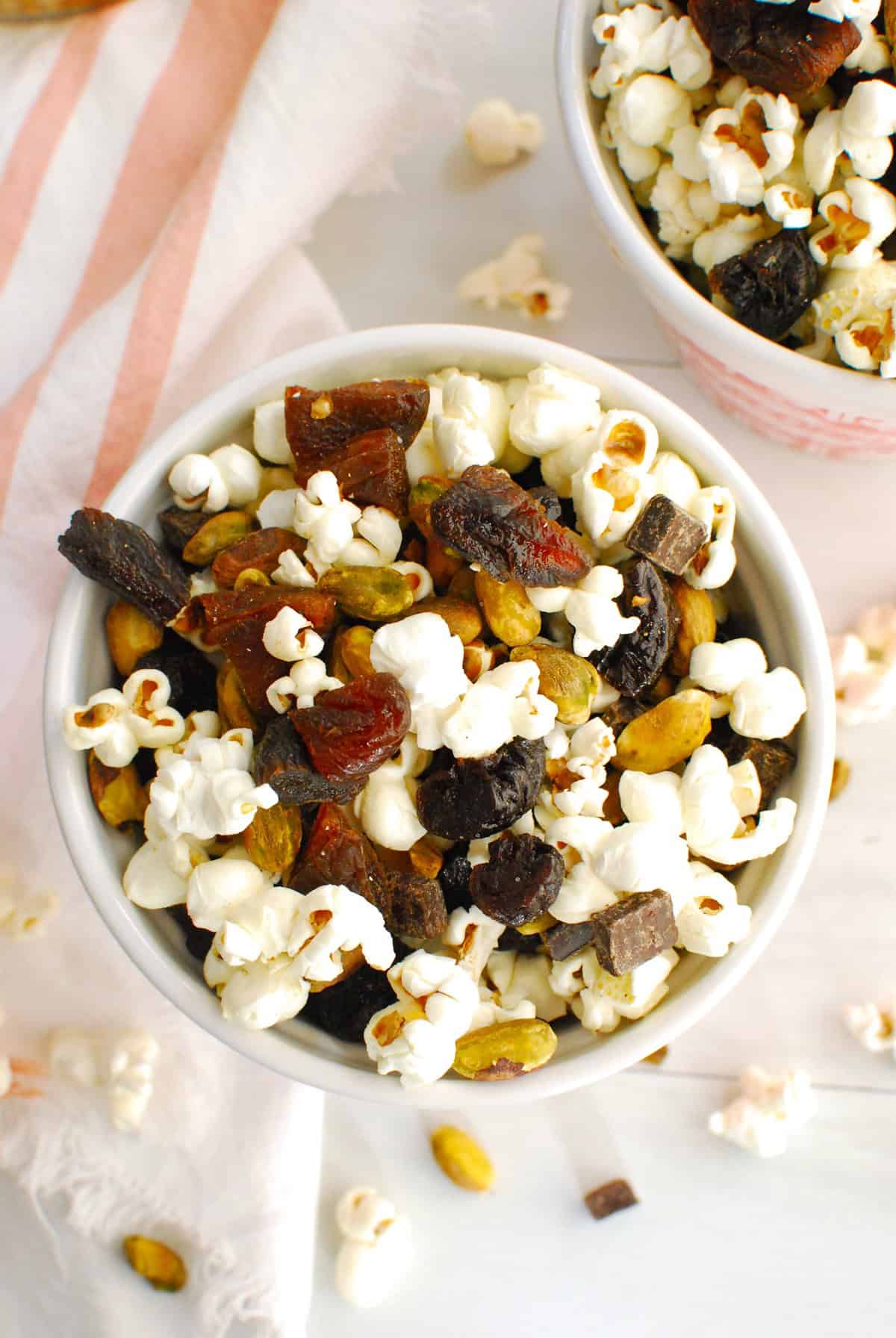 An overhead look at a bowl of popcorn trail mix, showing the popcorn, nuts, dried fruit, and chocolate.