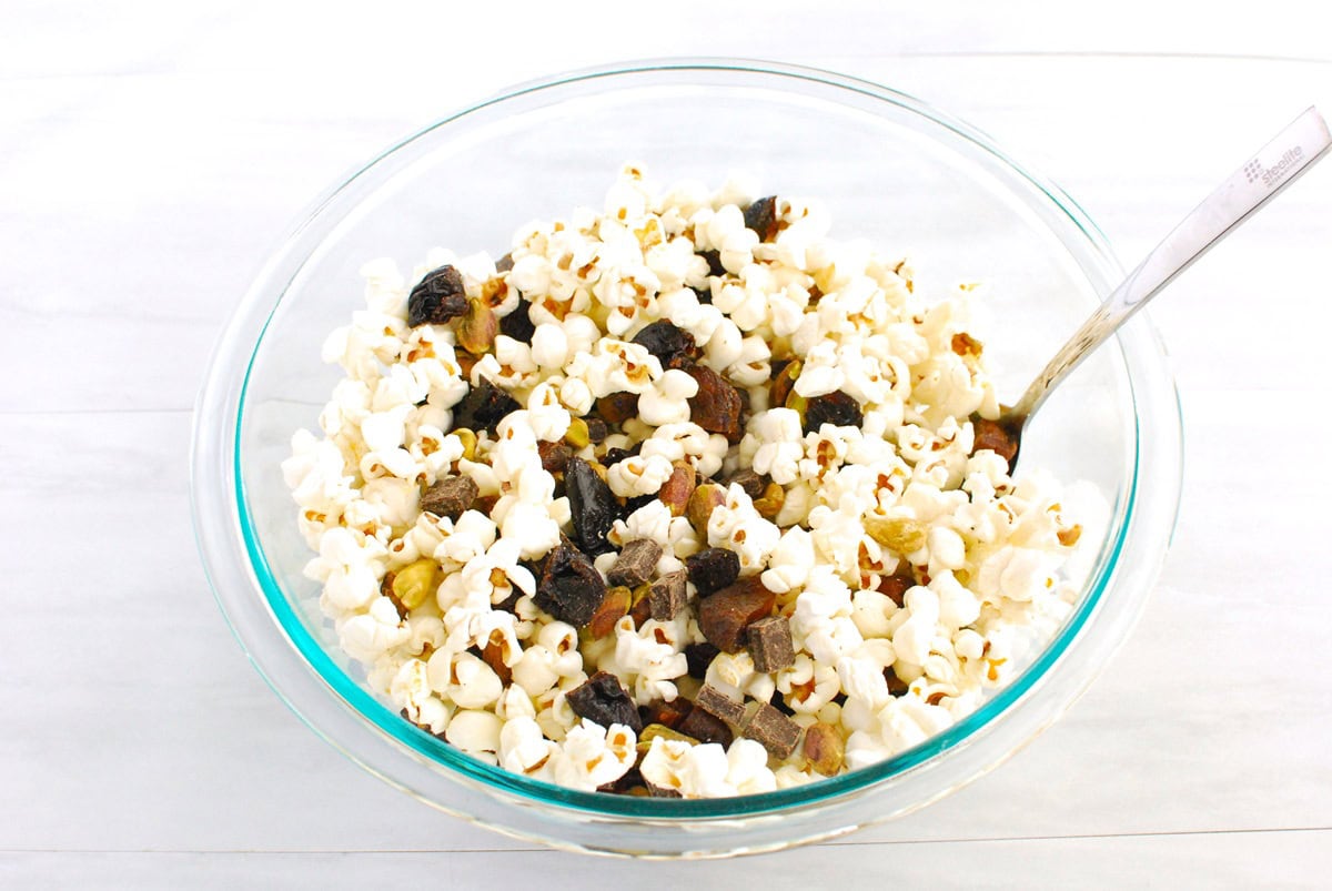 Popcorn in a mixing bowl with pistachios, prunes, apricots, and chocolate.