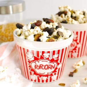 A bowl of popcorn trail mix next to a napkin and some popcorn kernels.