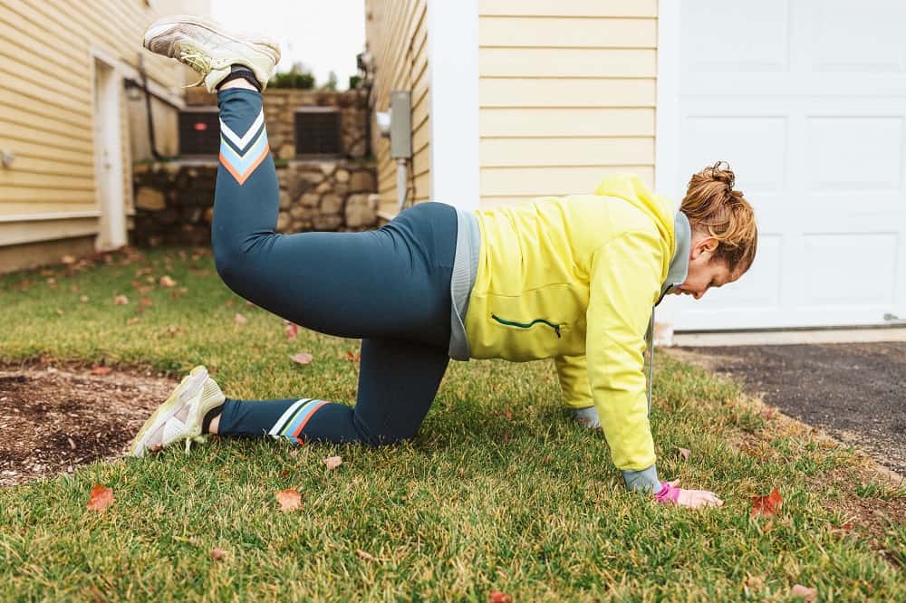 a woman doing donkey kicks exercise outside in the grass