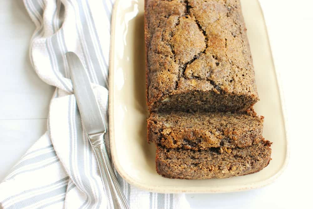 a loaf of buckwheat banana bread on a cream colored plate next to a napkin