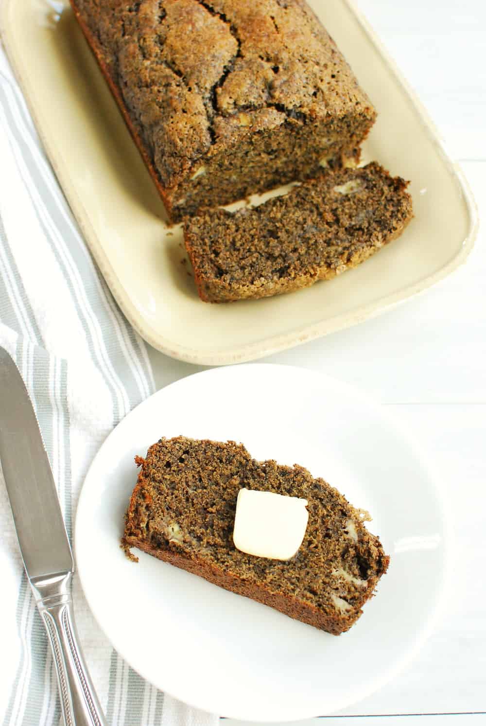 a slice of buckwheat banana bread with a pat of butter on a plate next to the rest of the loaf