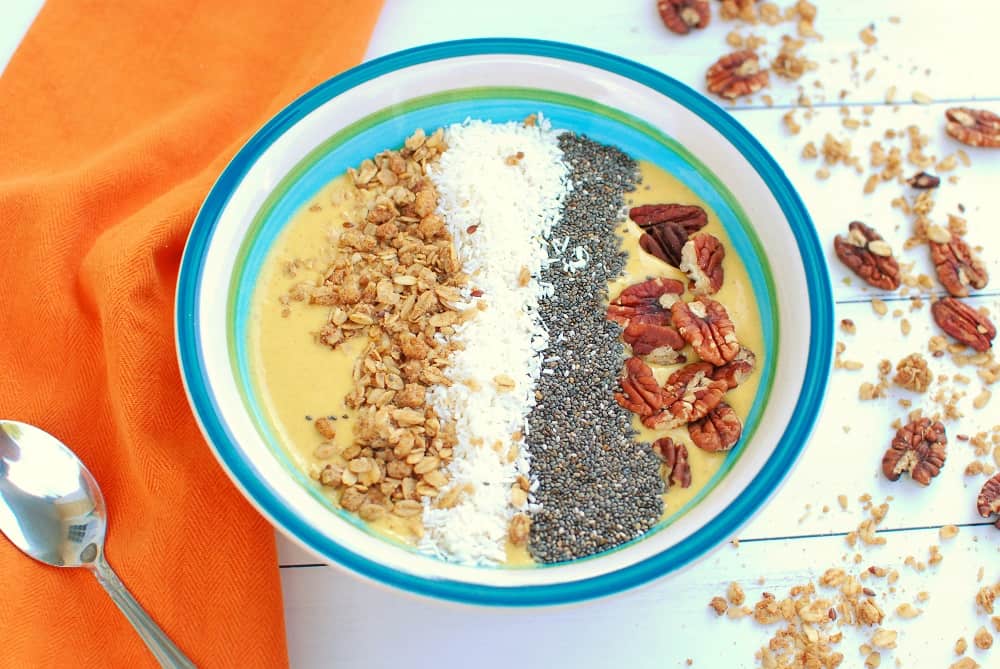 A pumpkin smoothie bowl topped with chia seeds, coconut, pecans, and granola.