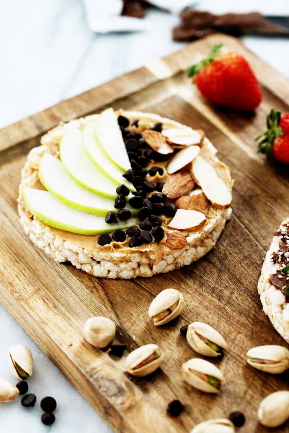 a rice cake topped with nut butter, apples, slivered almonds, and mini dark chocolate chips